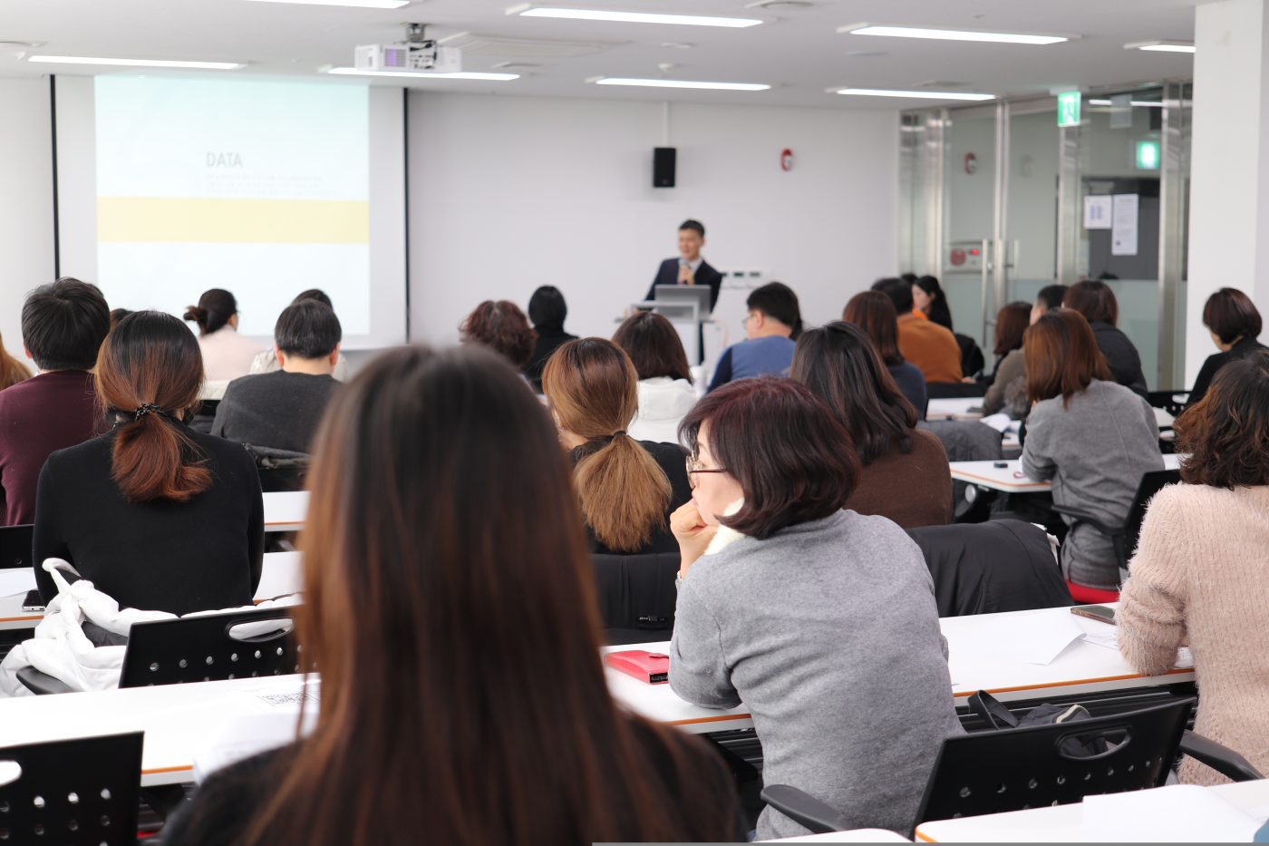 Speaker at a podium presenting to a full lecture hall, with a projection screen on the left showing a slide labeled DATA | PymesAutonomos.com