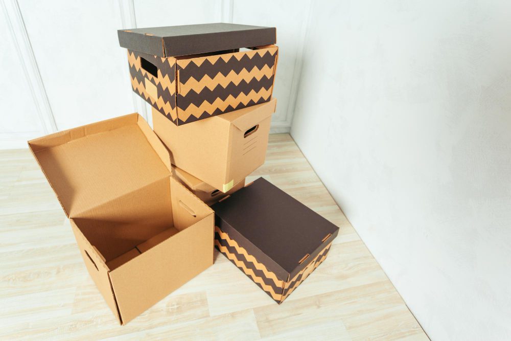 777899 - Cartonajes VAHL | PymesAutonomos.com Stack of cardboard moving boxes, including a chevron-patterned box on top, on a light wooden floor. | PymesAutonomos.com