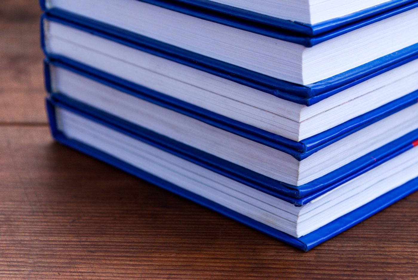Stack of books on wooden background | PymesAutonomos.com Stack of blue hardcover books stacked on a wooden table, viewed from the side. | PymesAutonomos.com