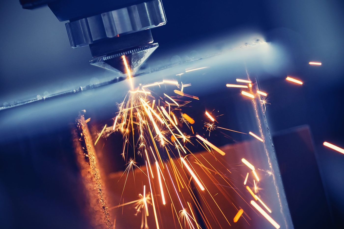 Laser cutting: a precision head emits a bright beam while orange sparks spray onto a metal sheet. | PymesAutonomos.com